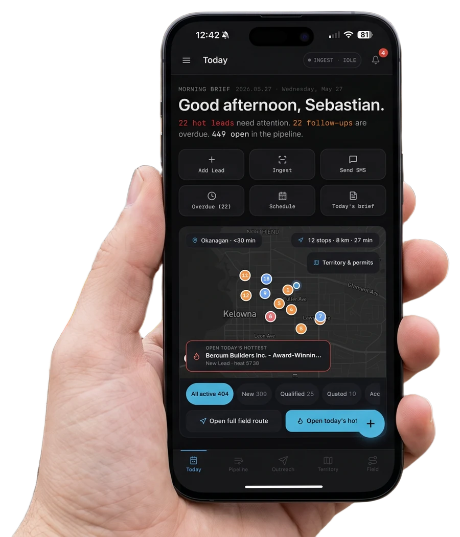 A dealer's hand holding a phone running the LeadX morning brief — hot leads, an Okanagan territory map, and today's ranked call-list — on a foundation job site